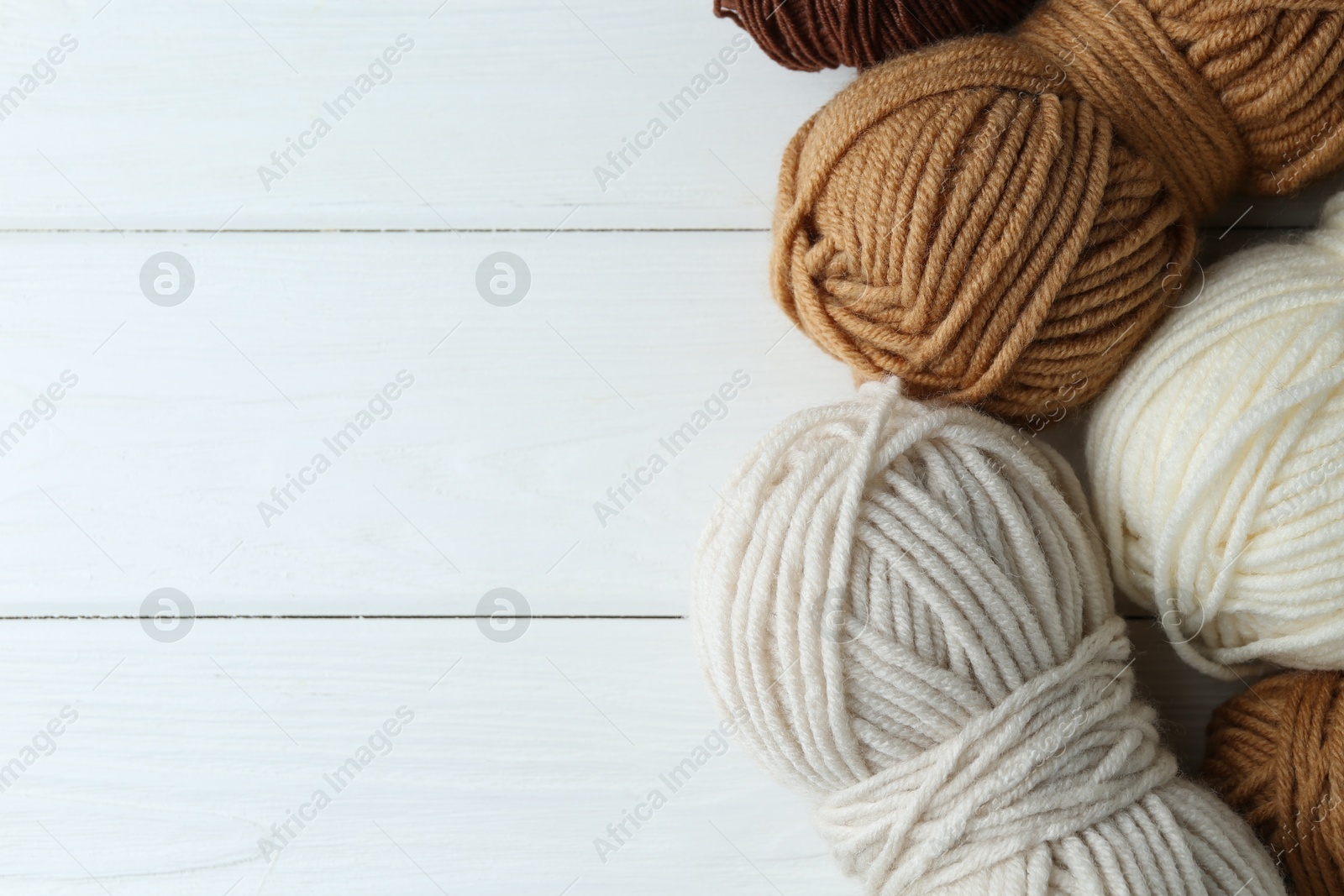 Photo of Skeins of different yarn on white wooden table, flat lay with space for text. Knitting material