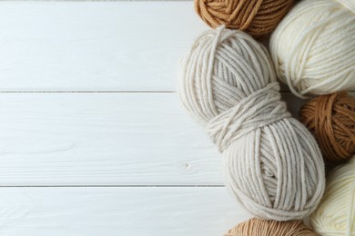 Photo of Skeins of different yarn on white wooden table, flat lay with space for text. Knitting material