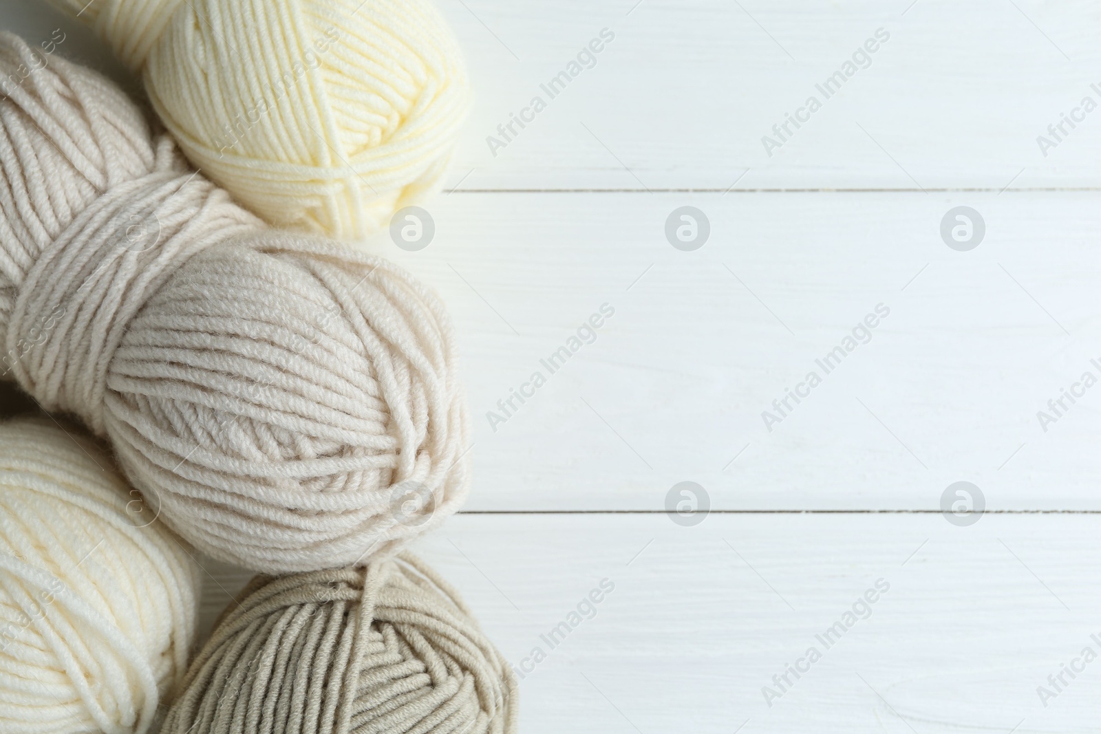 Photo of Skeins of different yarn on white wooden table, flat lay with space for text. Knitting material