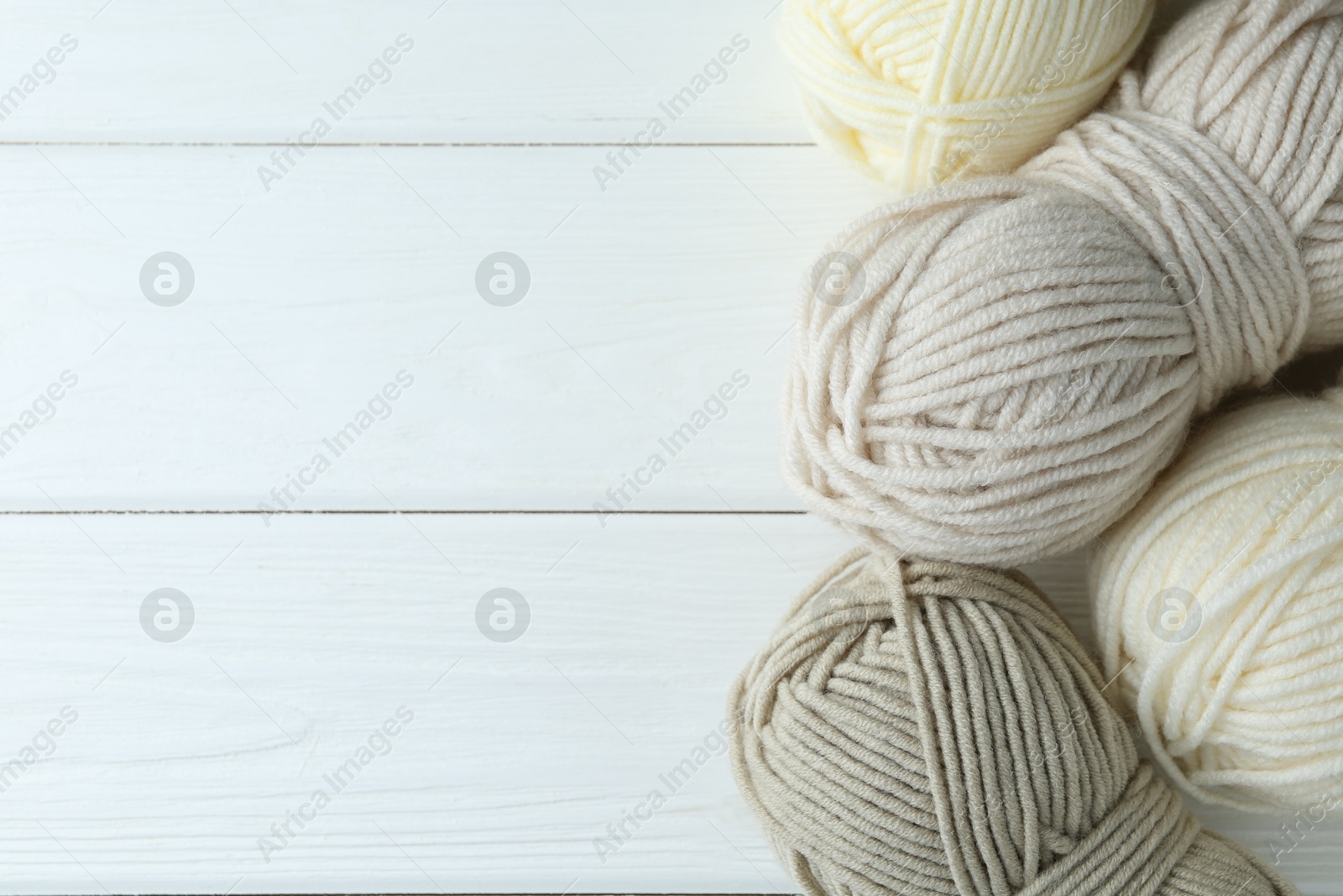 Photo of Skeins of different yarn on white wooden table, flat lay with space for text. Knitting material