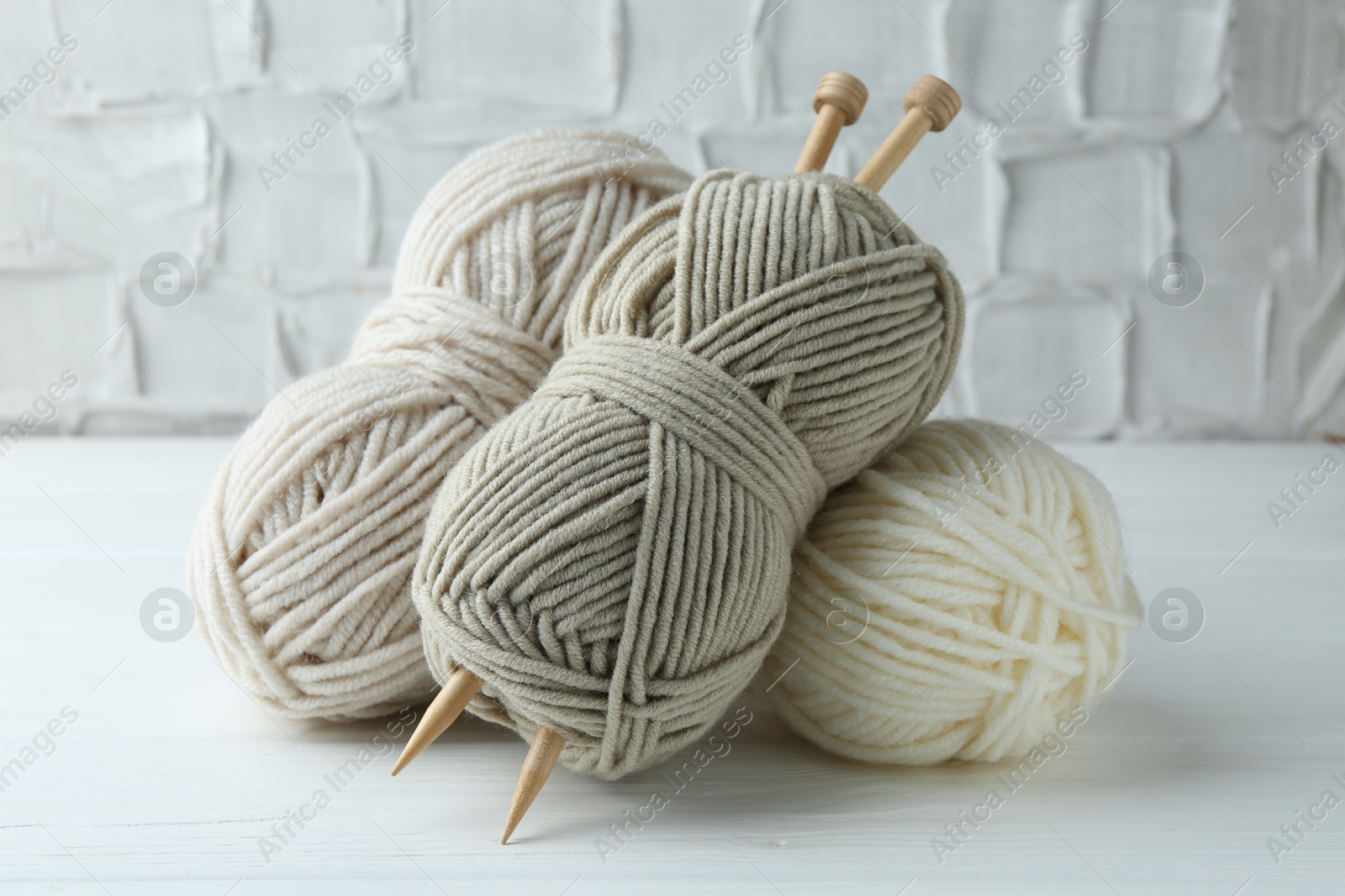 Photo of Skeins of different yarn and knitting needles on white wooden table, closeup