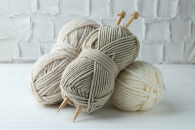 Photo of Skeins of different yarn and knitting needles on white wooden table, closeup