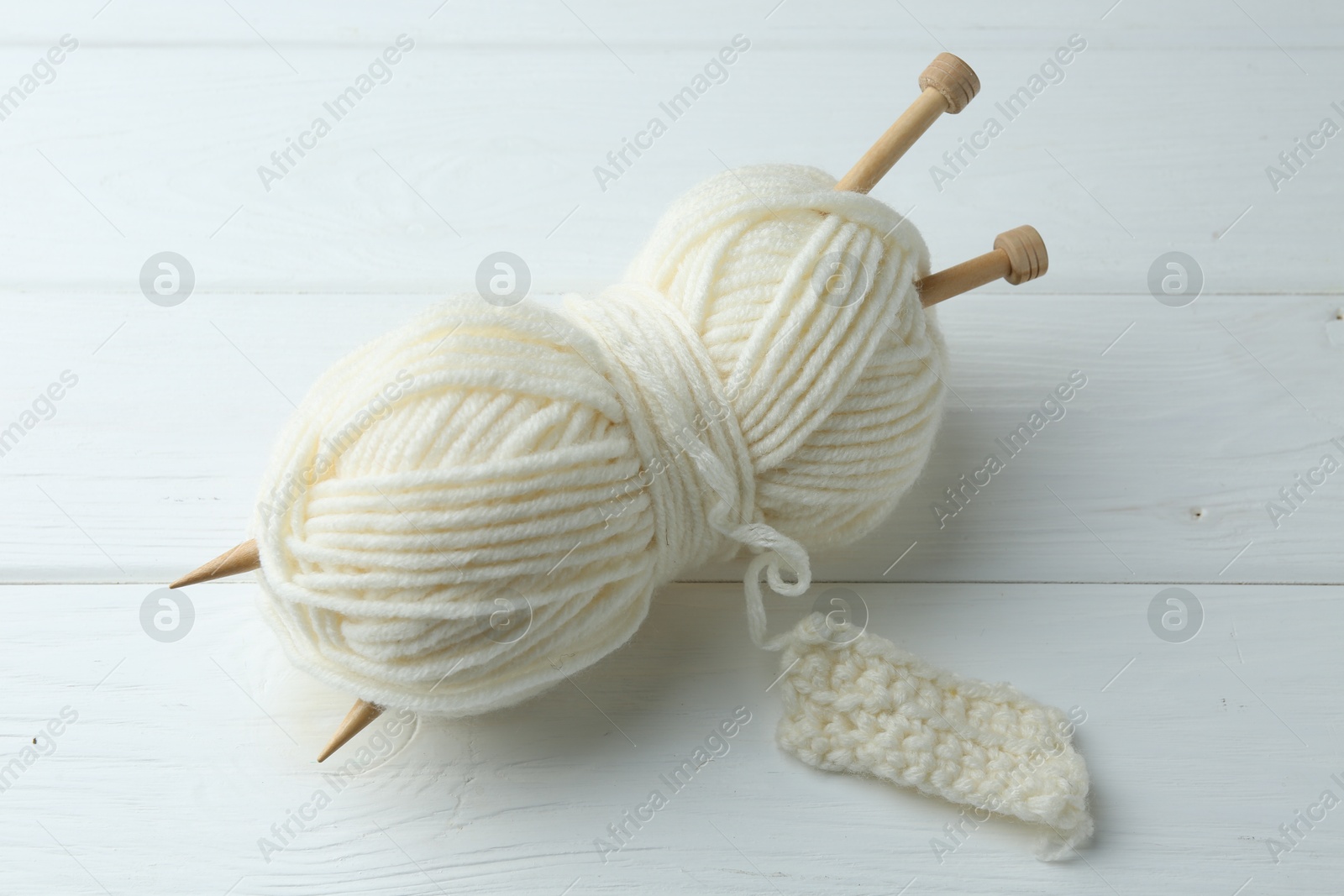 Photo of White yarn with knitting needles and pattern sample on wooden table