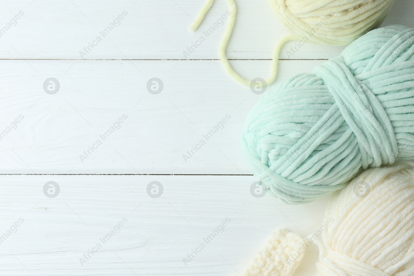 Photo of Skeins of yarn and pattern sample on white wooden table, flat lay. Space for text