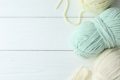 Skeins of yarn and pattern sample on white wooden table, flat lay. Space for text