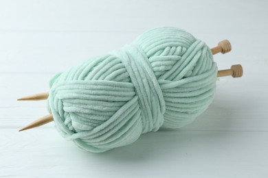 Photo of Plush yarn with knitting needles on white wooden table, closeup