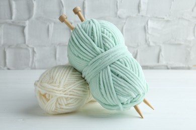 Photo of Skeins of yarn and knitting needles on white wooden table, closeup