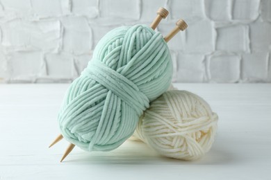 Photo of Skeins of yarn and knitting needles on white wooden table, closeup