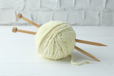 Ball of plush yarn with knitting needles on white wooden table, closeup