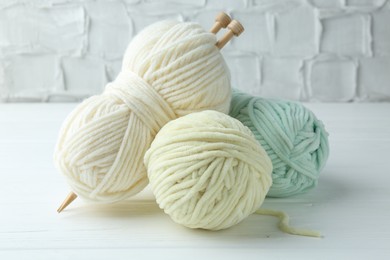 Skeins of different yarn and knitting needles on white wooden table, closeup