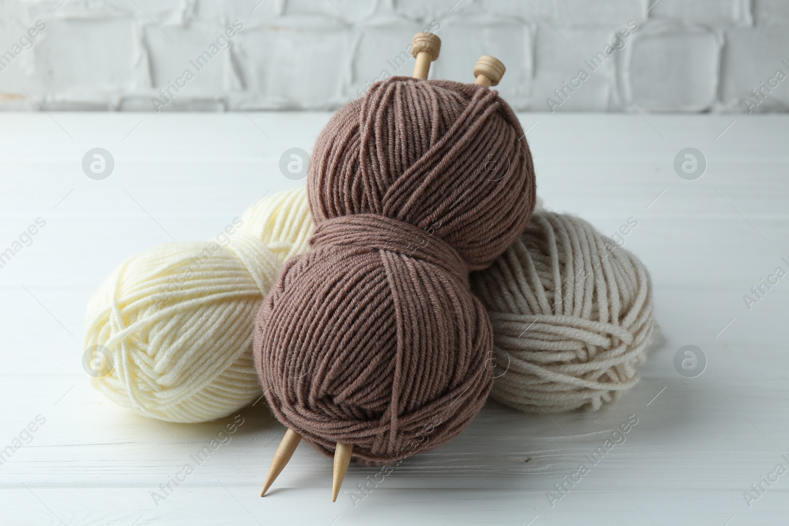 Photo of Skeins of yarn and knitting needles on white wooden table, closeup