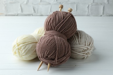 Photo of Skeins of yarn and knitting needles on white wooden table, closeup