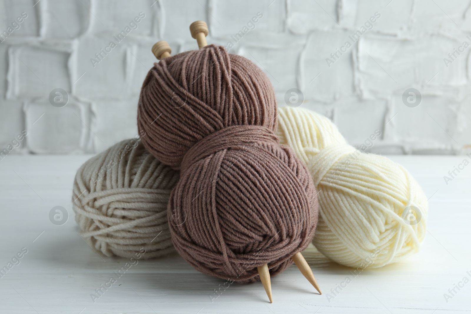 Photo of Skeins of yarn and knitting needles on white wooden table, closeup