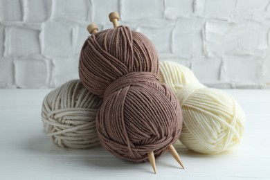 Skeins of yarn and knitting needles on white wooden table, closeup