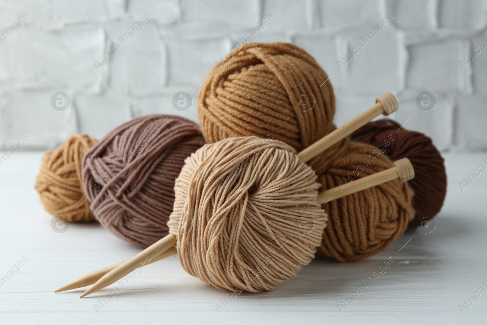 Photo of Skeins of different yarn and knitting needles on white wooden table, closeup