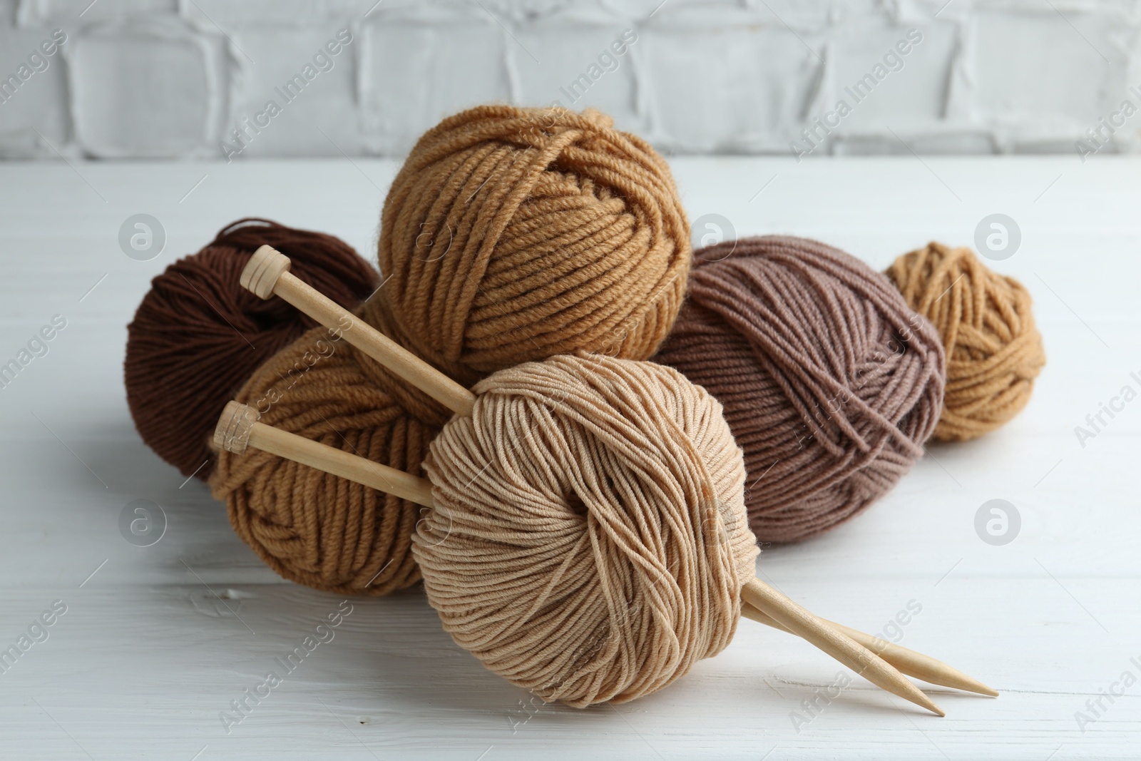 Photo of Skeins of different yarn and knitting needles on white wooden table, closeup