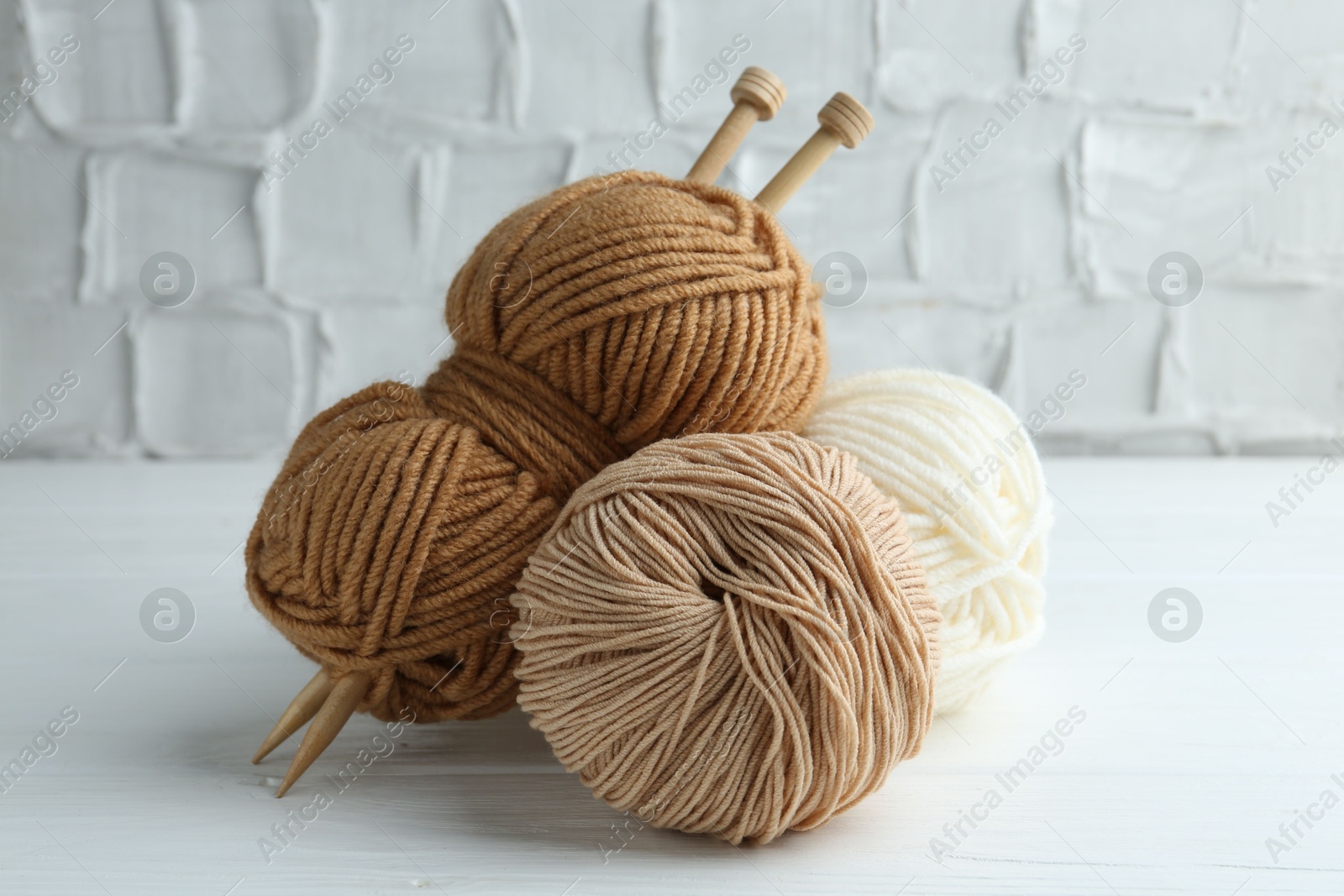 Photo of Skeins of different yarn and knitting needles on white wooden table, closeup