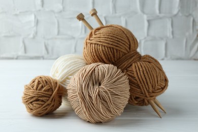 Skeins of different yarn and knitting needles on white wooden table, closeup