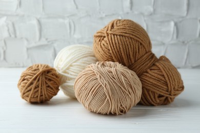 Photo of Skeins of different yarn on white wooden table, closeup. Knitting material