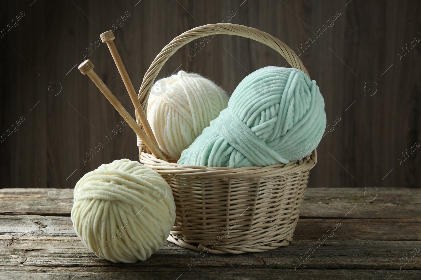 Photo of Skeins of yarn, knitting needles and wicker basket on wooden table, closeup