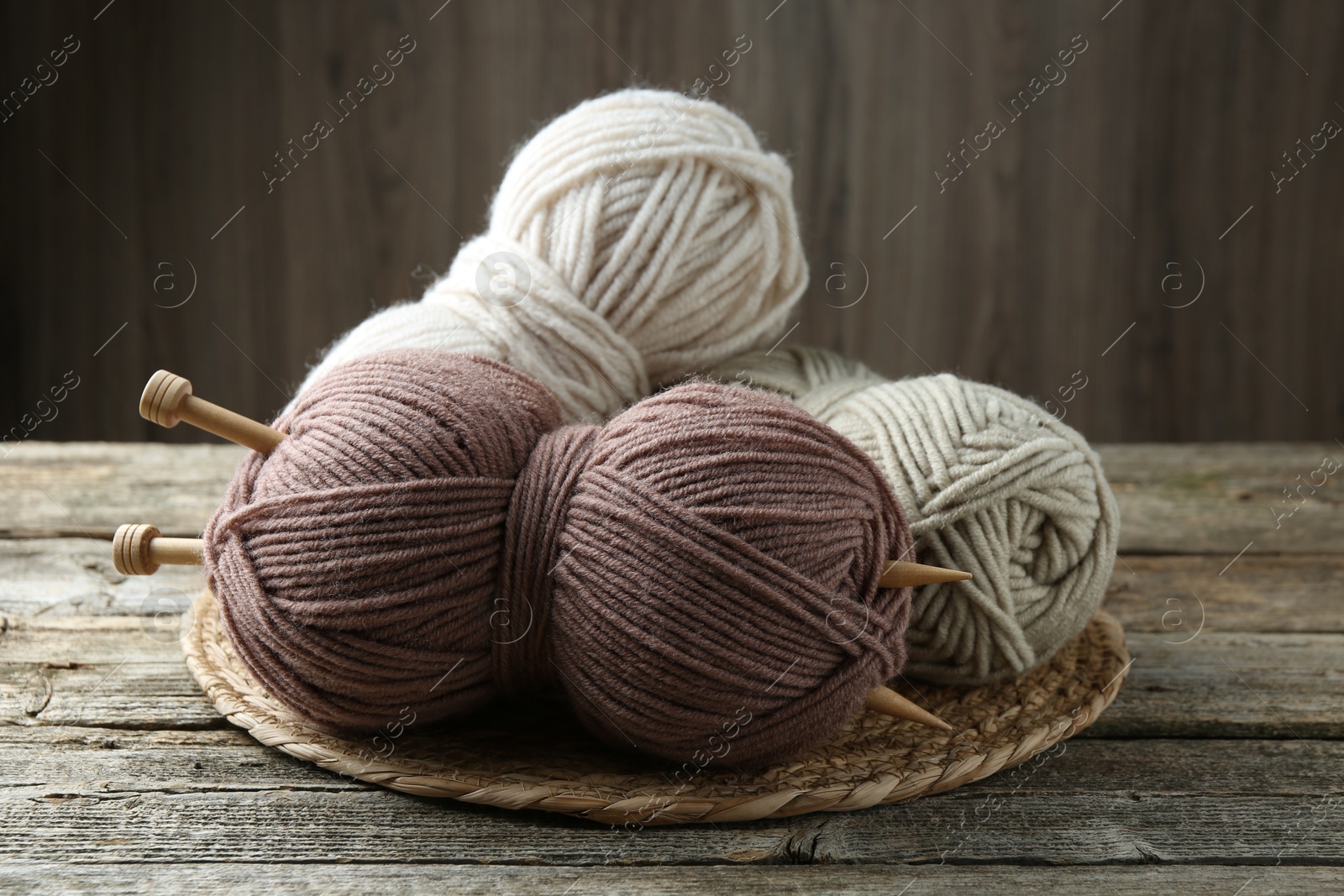 Photo of Skeins of yarn, knitting needles and wicker mat on wooden table, closeup