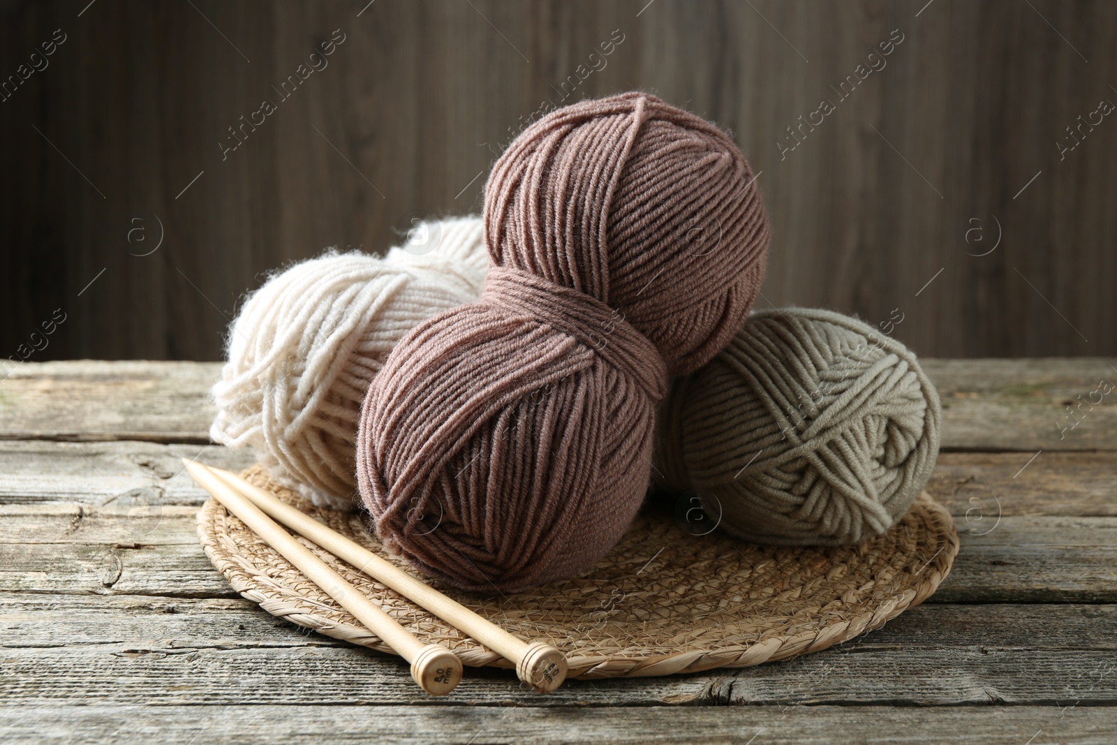 Photo of Skeins of yarn, knitting needles and wicker mat on wooden table, closeup