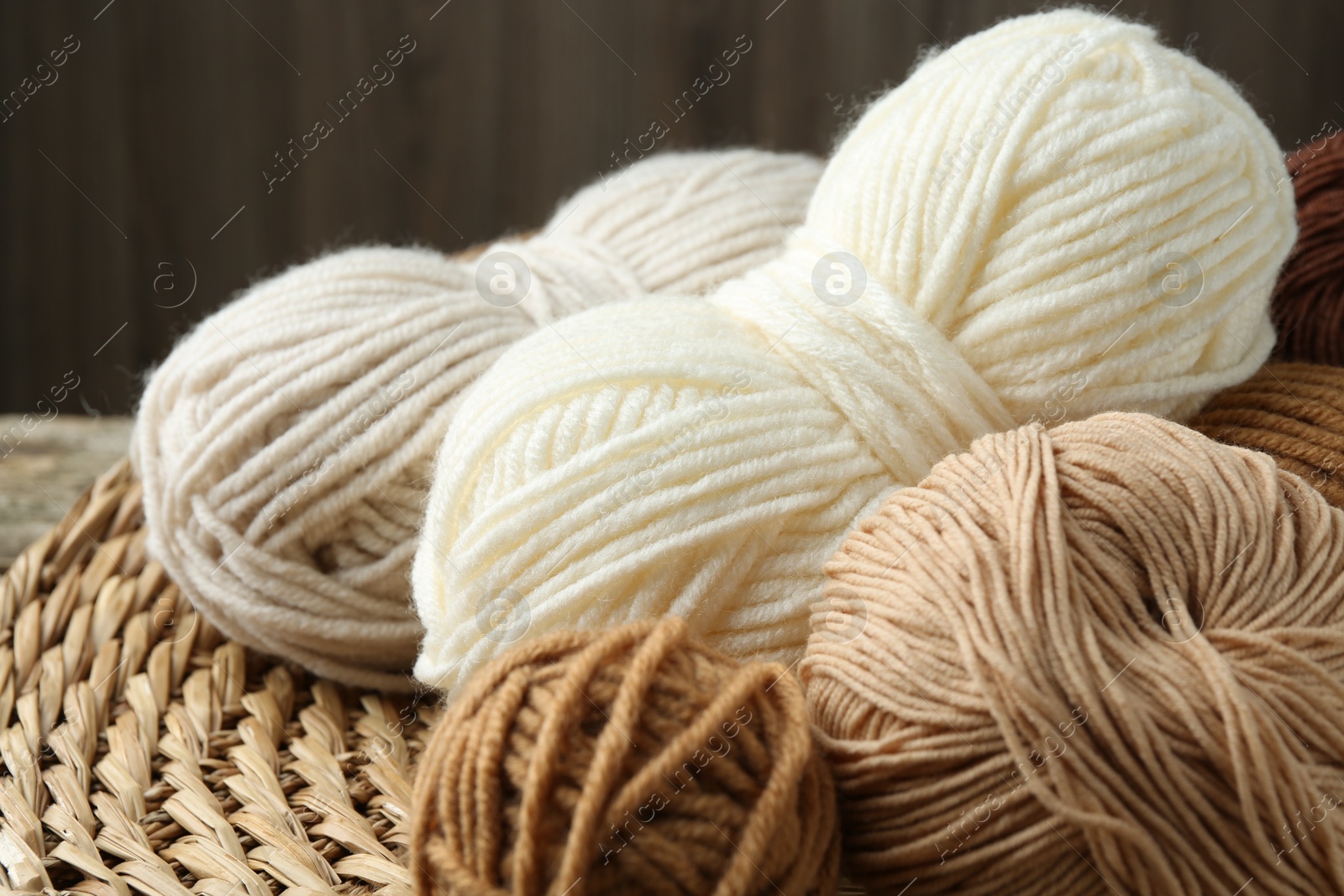 Photo of Skeins of different yarn and wicker mat on table, closeup. Knitting material