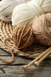 Skeins of yarn, knitting needles and wicker mat on wooden table, above view