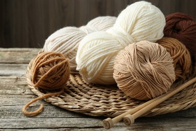 Photo of Skeins of yarn, knitting needles and wicker mat on wooden table, closeup