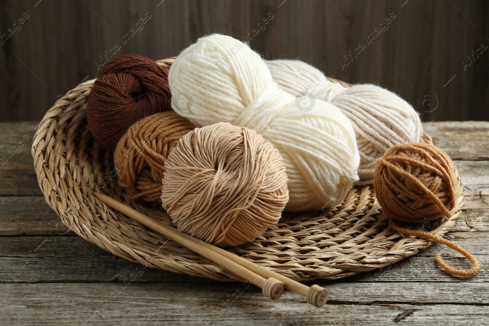 Photo of Skeins of yarn, knitting needles and wicker mat on wooden table, closeup