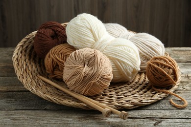 Skeins of yarn, knitting needles and wicker mat on wooden table, closeup