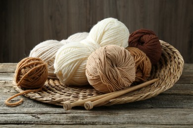 Photo of Skeins of yarn, knitting needles and wicker mat on wooden table, closeup