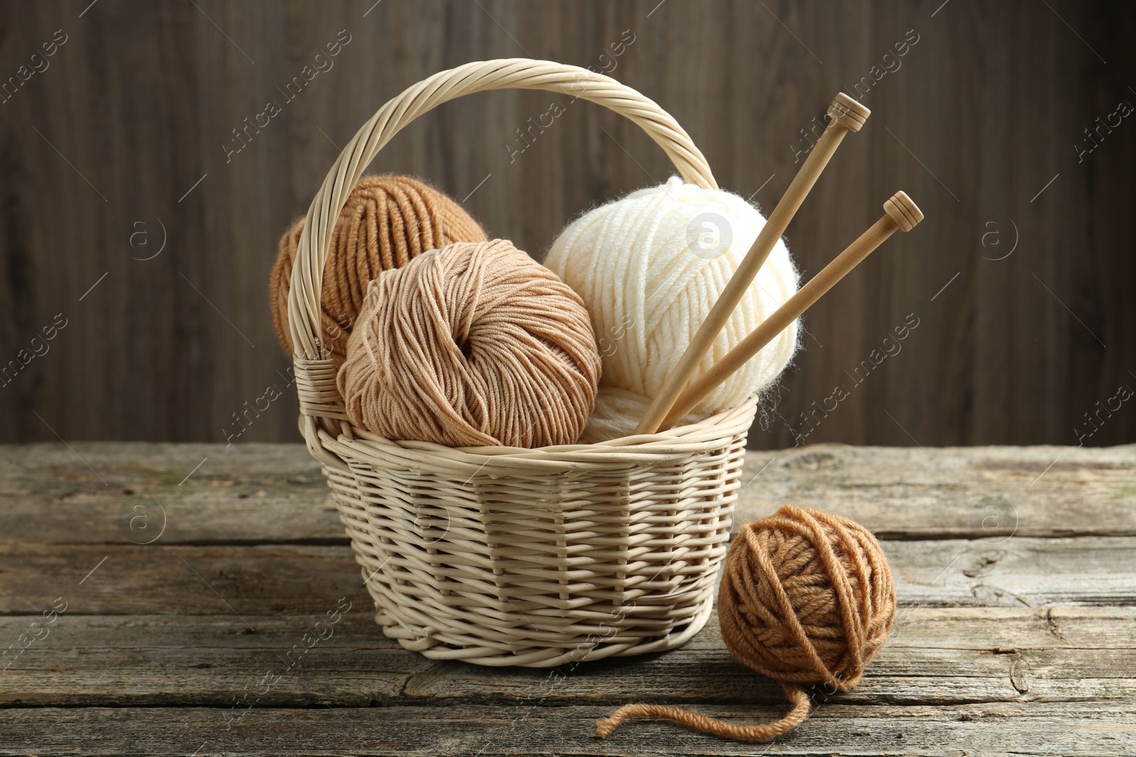 Photo of Skeins of yarn, knitting needles and wicker basket on wooden table, closeup