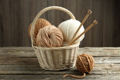 Photo of Skeins of yarn, knitting needles and wicker basket on wooden table, closeup