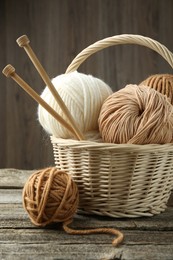 Skeins of yarn, knitting needles and wicker basket on wooden table, closeup