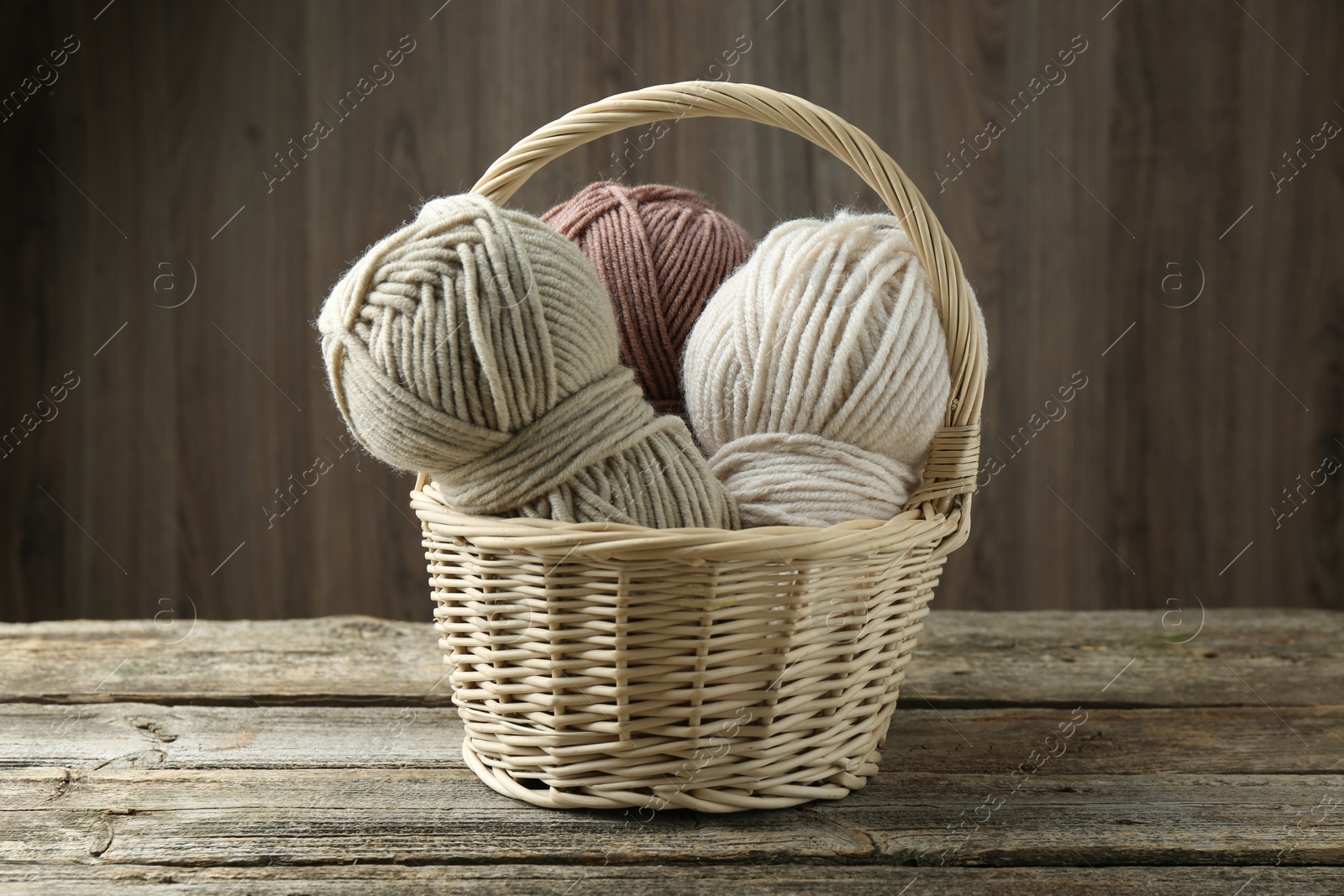 Photo of Skeins of different yarn in wicker basket on wooden table, closeup. Knitting material