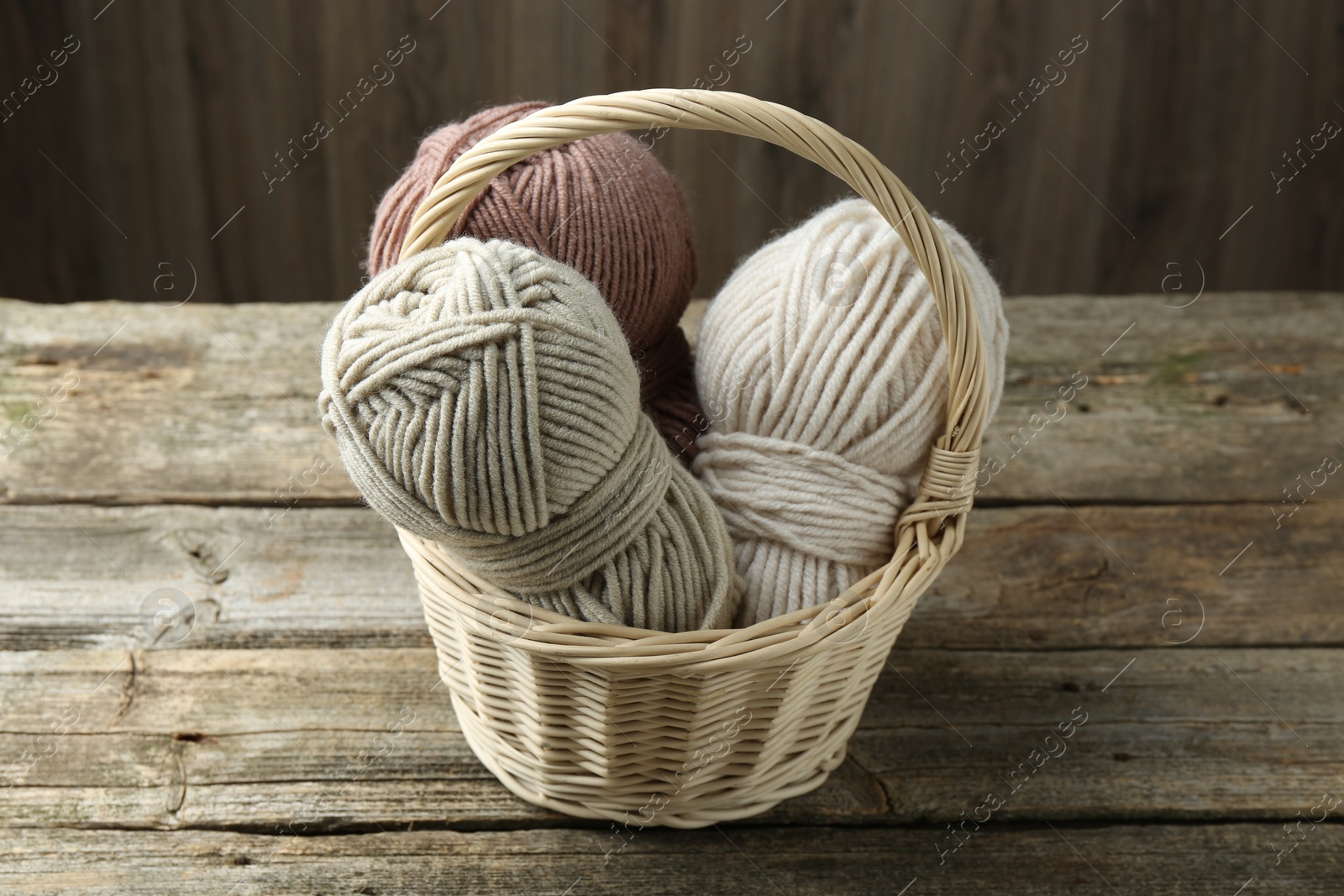 Photo of Skeins of different yarn in wicker basket on wooden table, closeup. Knitting material