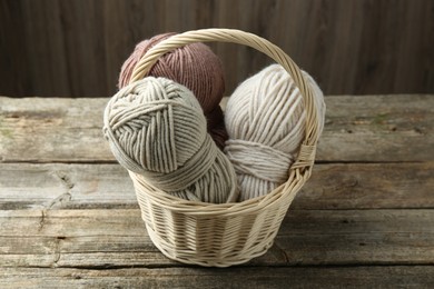 Photo of Skeins of different yarn in wicker basket on wooden table, closeup. Knitting material