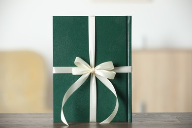 Book tied with beige ribbon as gift on wooden table indoors