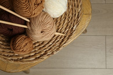 Photo of Skeins of yarn, knitting needles and wicker mat on chair indoors, top view. Space for text