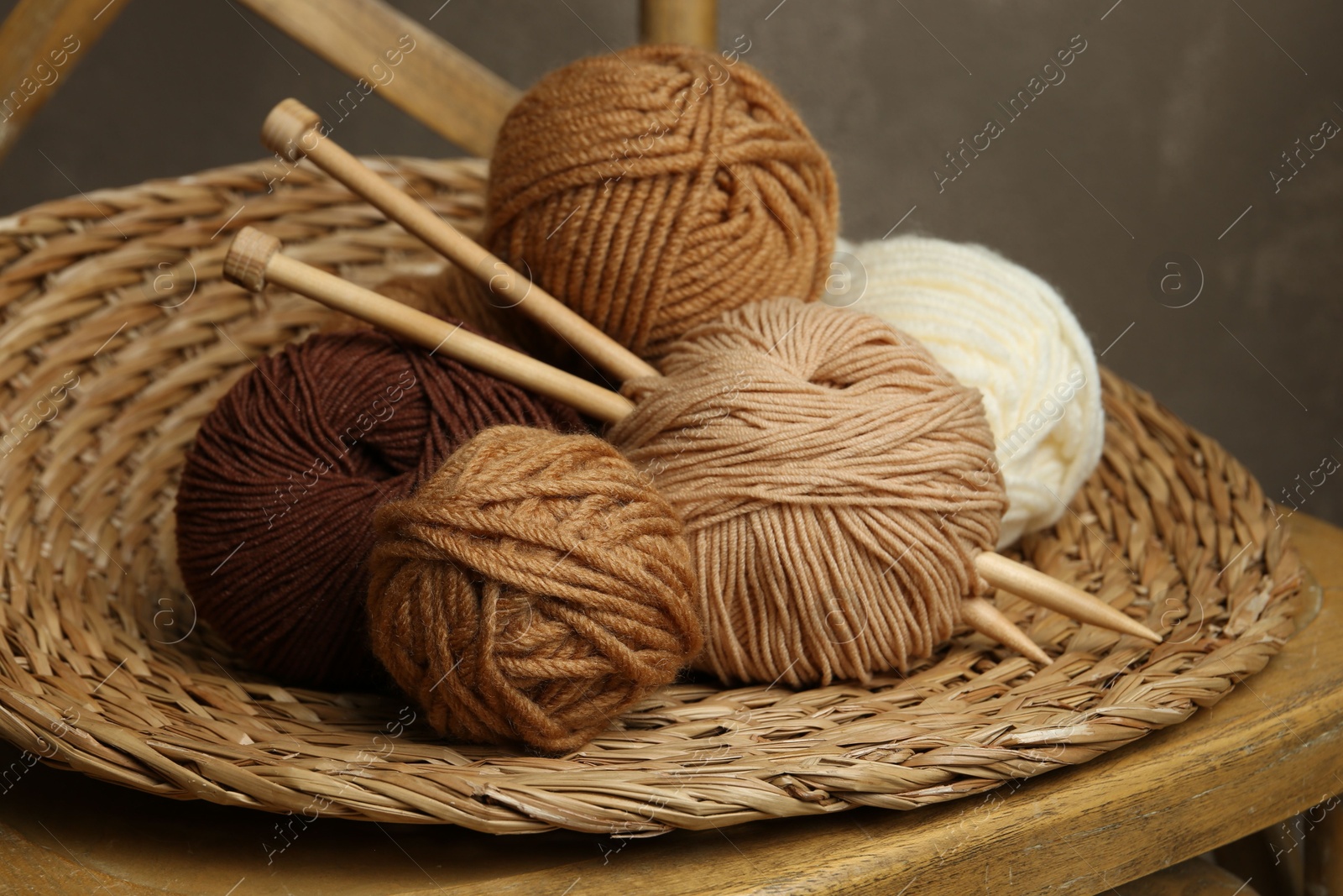 Photo of Skeins of different yarn, knitting needles and wicker mat on chair, closeup