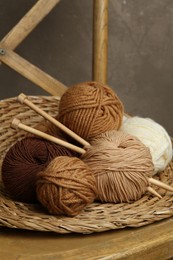 Photo of Skeins of different yarn, knitting needles and wicker mat on chair