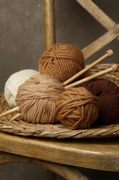 Photo of Skeins of different yarn, knitting needles and wicker mat on chair