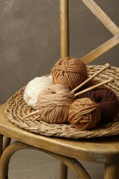 Skeins of different yarn, knitting needles and wicker mat on chair indoors