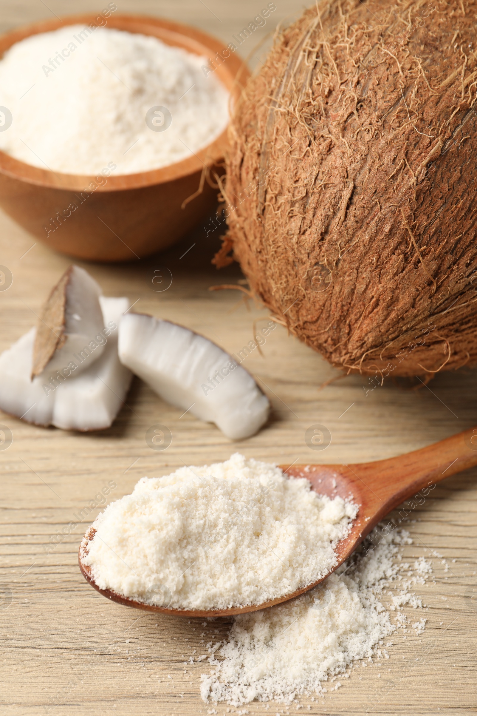 Fresh coconut flour in spoon, bowl and nuts on wooden table Photo of Fresh coconut flour in spoon, bowl and nuts on wooden table