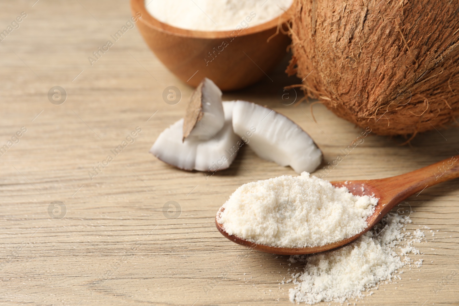 Photo of Fresh coconut flour in spoon, bowl and nuts on wooden table, space for text