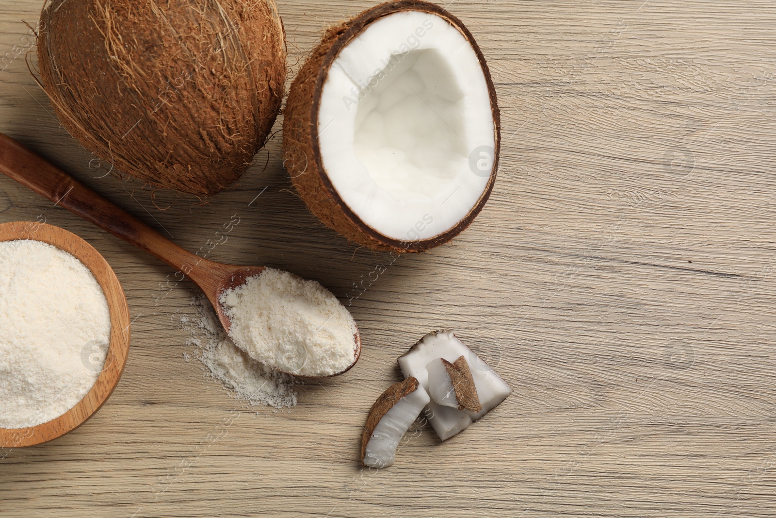 Photo of Fresh coconut flour in spoon, bowl and nuts on wooden table, flat lay. Space for text