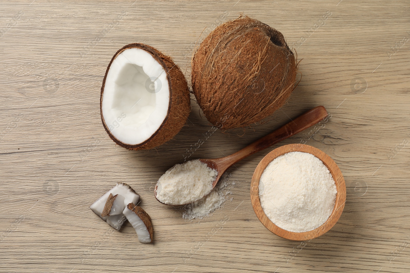 Photo of Fresh coconut flour in spoon, bowl and nuts on wooden table, flat lay