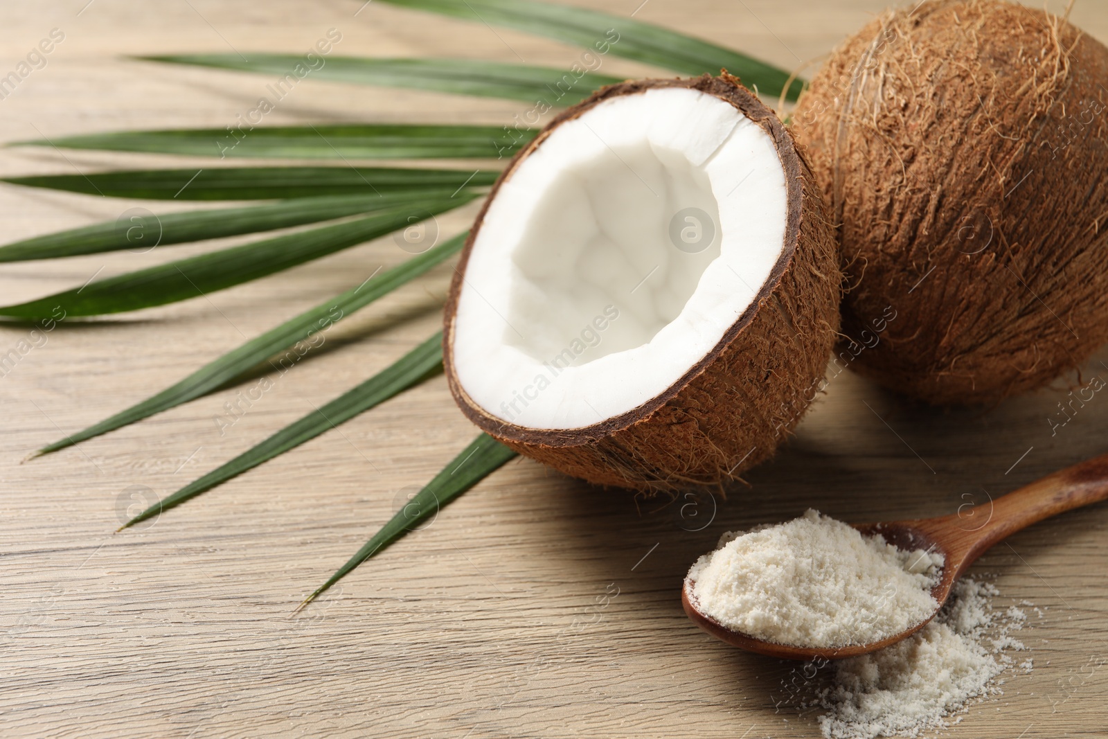 Photo of Fresh coconut flour in spoon, nuts and palm leaf on wooden table