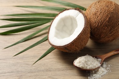 Photo of Fresh coconut flour in spoon, nuts and palm leaf on wooden table